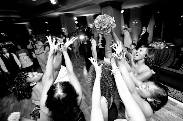 black and white photo -fun photo of the single ladies at the reception all reaching to catch the bride's bouquet - photo by Houston based wedding photographer Adam Nyholt